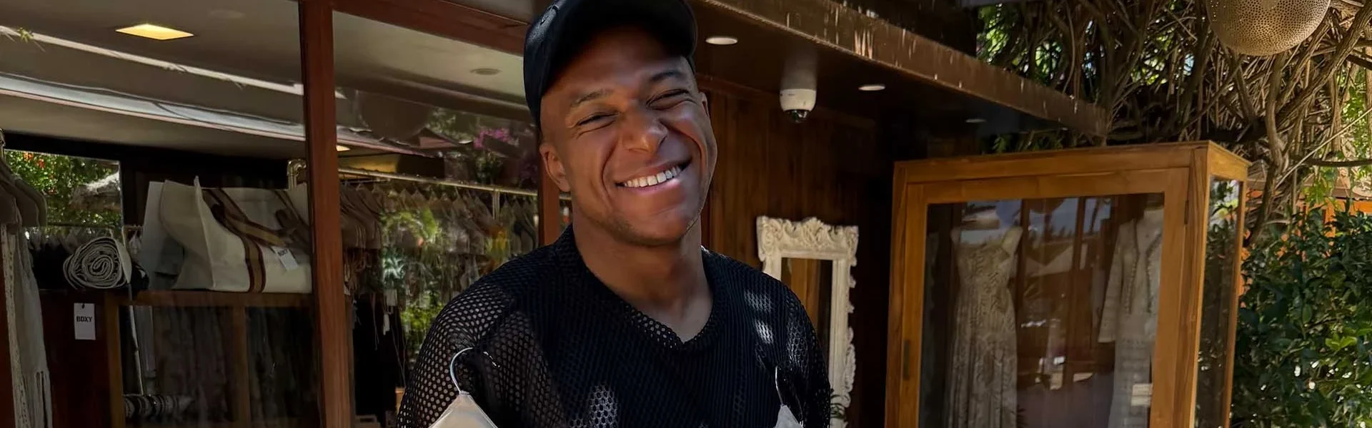 Mbappé poses smiling with several women's garments hanging on hangers. | Instagram